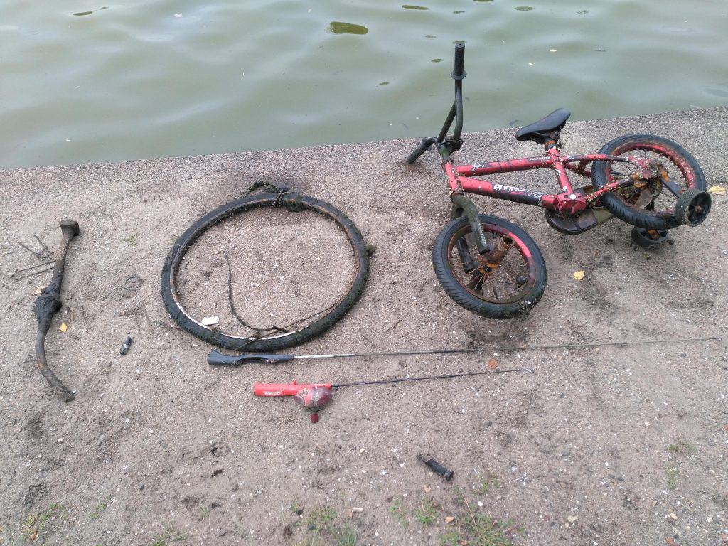 Dětské kolo, ráfek a udice na kamenitém břehu